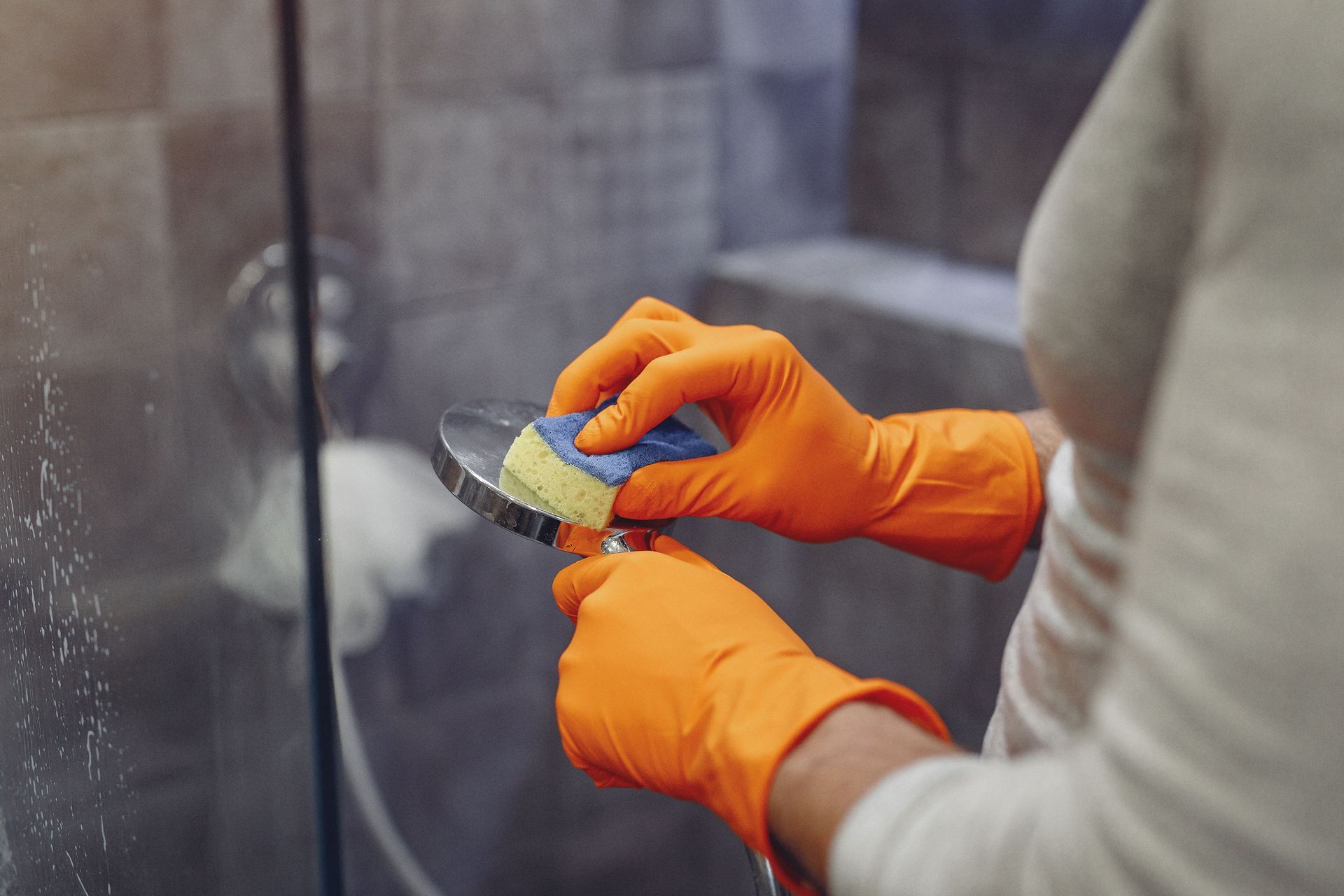 Crop faceless male in orange rubber gloves wiping by sponge shower nozzle